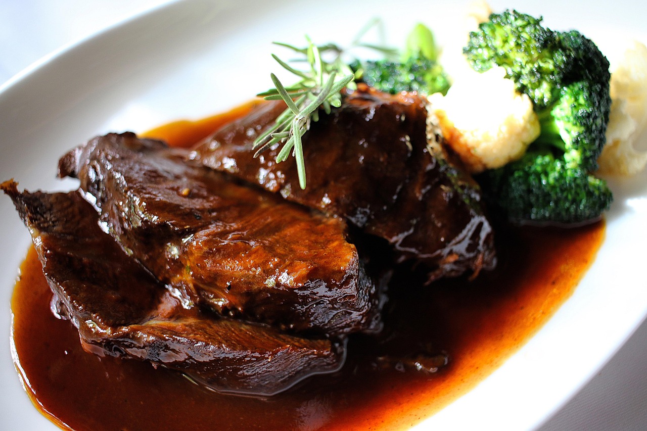 Brasato al vino rosso servito su un piatto, con contorni di verdure e una spruzzata di prezzemolo fresco.