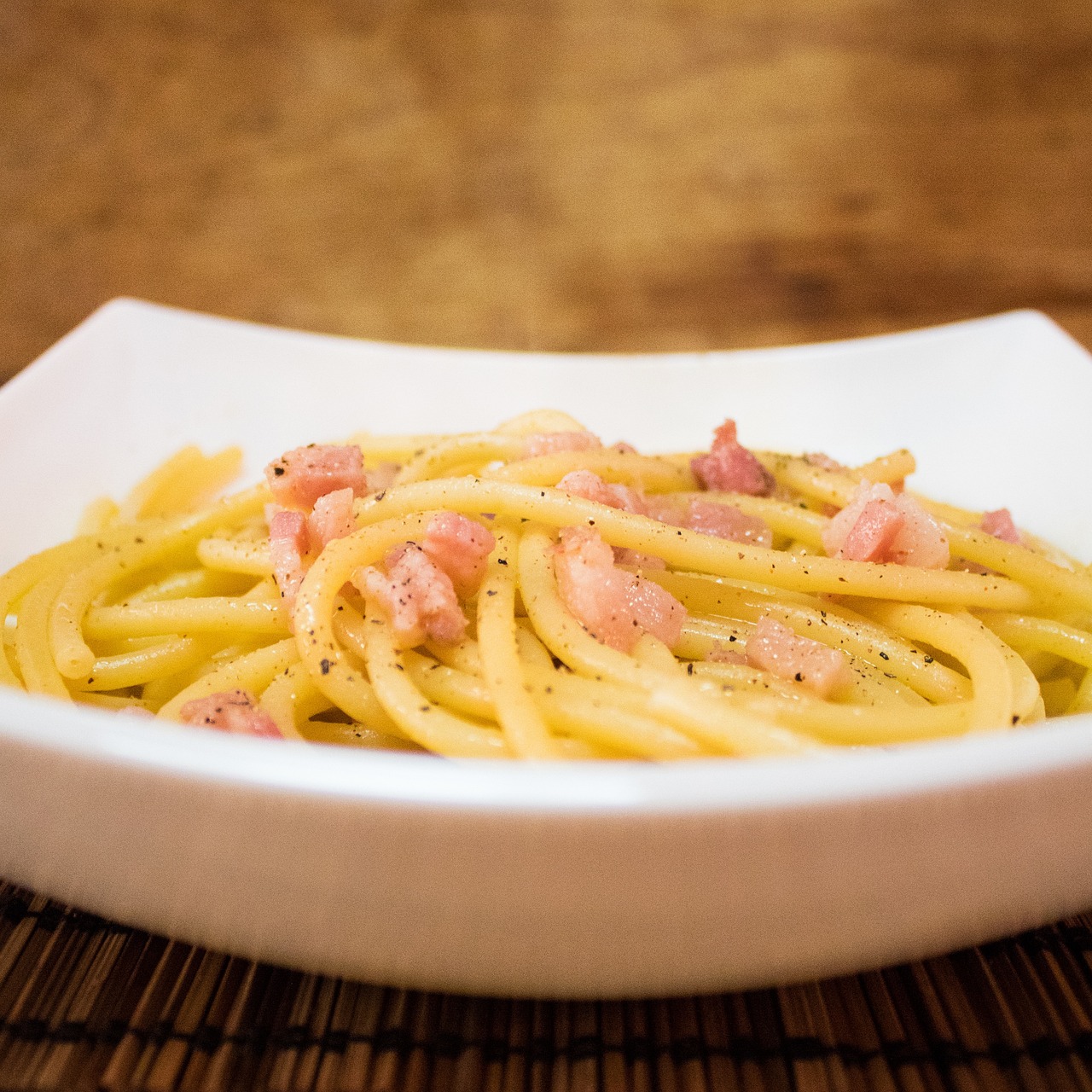 Pasta alla carbonara con crema densa, guanciale croccante e spolverata di pepe nero.
